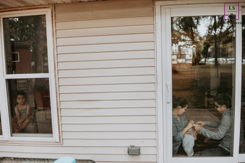 Window to a New Chapter: Family Love in Mahomet In Mahomet, IL, a serene lifestyle portrait. A couple sit side by side, caring for their precious newborn, while their firstborn gazes peacefully through the window. The beauty of family and love is beautifully showcased in this setting.