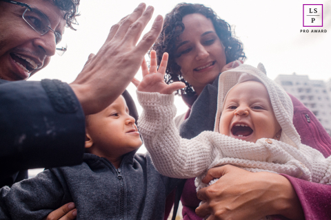 Uma família alegre em São Paulo, Brasil, passando um tempo de qualidade juntos no parque. O pai dá um high five em seu bebê, enquanto a mãe amorosamente segura o pequeno. Um menino pequeno fica por perto, juntando-se ansiosamente ao divertido retrato de família.