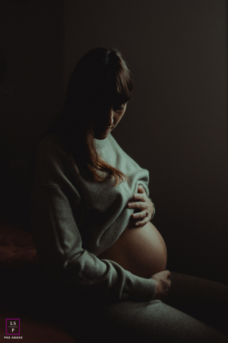In Montecatini Terme, Pistoia, Toscana, Italy, a maternity profile is softly illuminated, capturing an expectant mother tenderly holding her belly. The gentle light enhances the warmth and beauty of this precious phase.