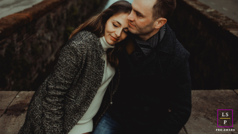 In Lucca, Toscana, Italia, a tender portrait captures a couple by the water. She leans into him, reflecting their deep connection and affection amidst the picturesque surroundings.