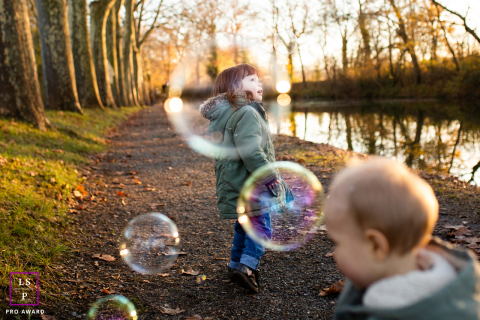 Les enfants savourent le charme de l'automne au bord de l'eau en Haute-Garonne Un charmant portrait de jeunes enfants de Haute-Garonne, jouant avec des bulles au bord de l'eau par le temps frais de l'automne.