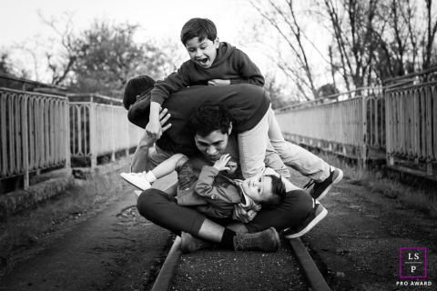 Un père et ses enfants partagent des moments ludiques sur les pistes du Tarn-et-Garonne Une image en noir et blanc capturant la joie de la paternité, alors qu'un père joue avec ses enfants sur des voies ferrées à voie étroite dans le Tarn-et-Garonne.