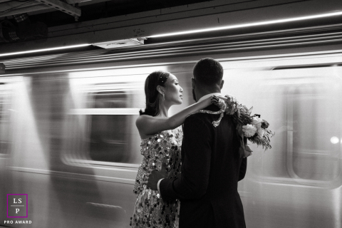 In Brooklyn, NY, a black and white photo session captures a couple in the subway, with the motion of the train passing by. The dynamic shot highlights their connection amidst the bustling urban backdrop.