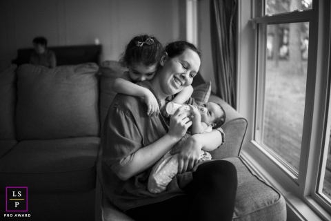 Mother Feeds Newborn While Older Child Shares Heartfelt Hug in Champaign, IL In Champaign, IL, a beautiful scene captures a mom feeding her newborn as her older child lovingly wraps her arms around her, filled with love and connection.