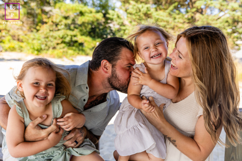 Tickles and Giggles: A Sun-Drenched Family Portrait in Yarmouth, Massachusetts Yarmouth, Massachusetts, USA | A mother and father are tickling and kissing their daughters. The sun-drenched photo is filled with laughter.