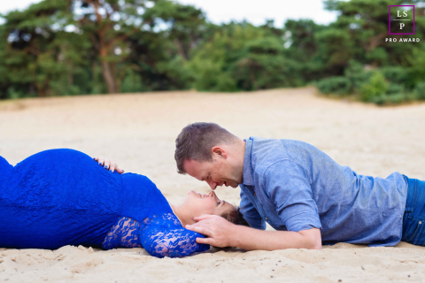 Un couple enceinte est allongé sur le sable d'Overijssel, aux Pays-Bas. Ils se regardent et rient. Leurs corps sont détendus et ils profitent ensemble d'un après-midi calme et intime.
