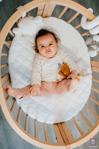 A top-down view of a baby happily lying on their back in a round crib. The photo, taken in Evian, shows the baby enjoying their new bed.