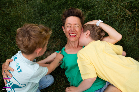 Souriante, une mère se repose sur l'herbe tandis que son fils joue à proximité Un portrait d'art de vivre du Tarn-et-Garonne montre une mère et son fils partageant une complicité profonde. La mère est allongée sur le dos dans l'herbe, souriante tandis que ses enfants jouent.