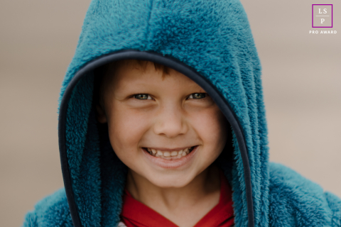 On a windswept Northern California beach, a blue-eyed boy in a cozy blue hoodie smiles joyfully.