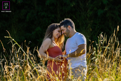 In Bardos, a couple of expectant parents stands face to face, warmly backlit and framed by dry grass. The sunlight creates a soft, golden glow, highlighting their anticipation and connection.