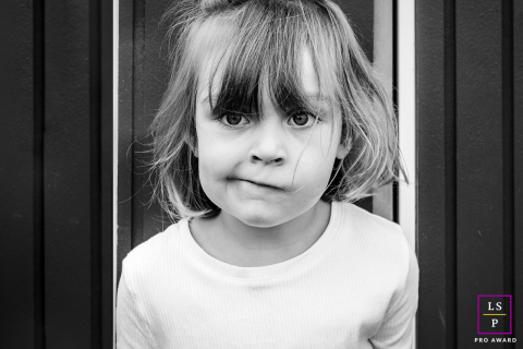 In Bayonne, France, a black and white tight portrait captures a young girl looking at the camera with an inquisitive gaze and a slanted, playful smile, highlighting her expressive and curious personality.