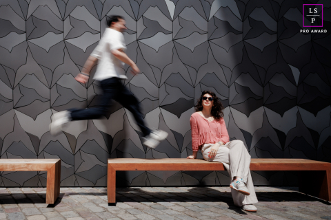 Mouvement à Paris : Sa sérénité, son saut, un portrait intemporel À Paris, en France, le portrait d'un couple élégant la montre assise élégamment sur un banc en bois, tandis qu'il saute d'un banc à l'autre. Le flou de mouvement dû à une obturation lente capture son mouvement dynamique à ses côtés.
