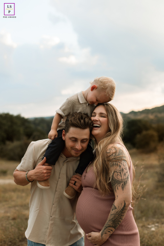 In San Antonio, Texas, a pregnant mom stands outdoors beside her husband, who carries their young son on his shoulders. The family enjoys a joyful, connected session in a natural setting.