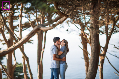 Baiser de San Francisco : l'affection romantique d'un couple sur le littoral À San Francisco, en Californie, un couple s'embrasse entouré d'arbres au bord de l'eau. La scène capture leur affection, les branches feuillues et le calme du rivage créant un décor romantique.