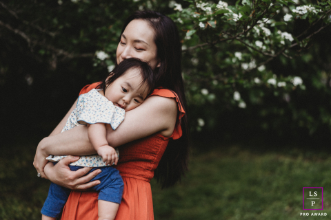 À Boston, dans le Massachusetts, une maman tient tendrement son enfant sous les arbres. Une douce lumière filtre à travers les feuilles, soulignant leur lien étroit dans ce cadre extérieur paisible et nourrissant.