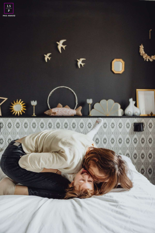 In Lyon, Auvergne Rhône-Alpes, France, a mother and daughter share a playful exchange of kisses, their faces close together, laughing and smiling in a warm display of affection.