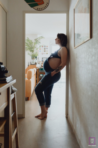 In Lyon, Auvergne Rhône-Alpes, France, an expectant mother stands in profile with her back against a wall, gently accentuating her pregnancy curves in a graceful, contemplative pose.