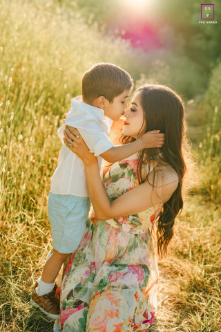 In golden sunlight at Ed R. Levin County Park, a little boy gently holds his mom’s face and kisses her on the nose. The backlighting creates warm, glowing tones around them.