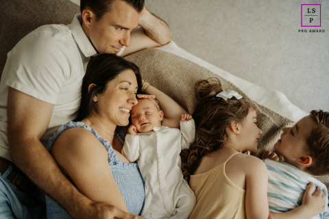In Portland, OR, a family enjoys a relaxed session together. Mom and dad lounge on a couch, smiling and cozy, with their three young children playing and cuddling beside them.