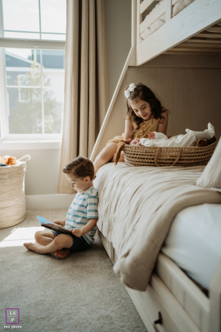 In Portland, OR, a toddler girl sits on the lower bunk bed beside a baby resting in a basket. Nearby, a young boy sits on the floor playing, capturing a cozy, welcoming family scene.
