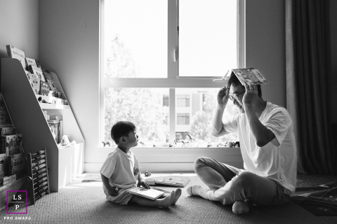 In a cozy Northern California home in Los Gatos, a father playfully balances a book on his head while reading to his young child, both sharing a joyful, lighthearted moment together.