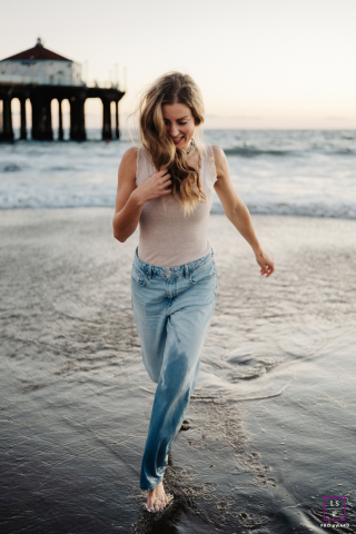 At Manhattan Beach, a woman runs through the tidal shallows by the ocean, her carefree laughter captured at sunset as waves crash the evening light.