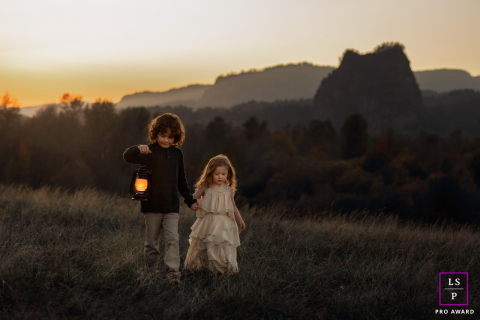 In Portland, Oregon, children carry a lantern across a hillside at dusk, illuminated by warm sunset tones as evening settles over the landscape.