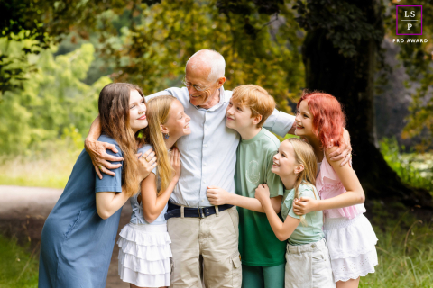 In Overijssel, Netherlands, a grandfather hugs all five of his grandchildren at once outdoors, surrounded by trees and natural scenery.