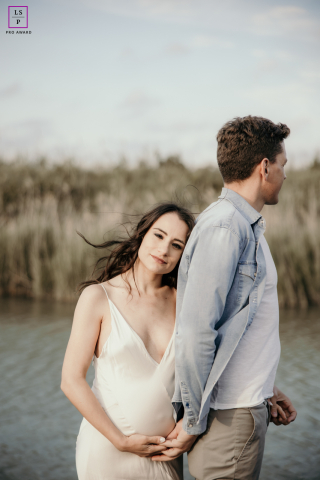 At Ravenna Wildlife Sanctuary in Italy, a candid maternity portrait shows a couple embracing in nature; he faces away as she nestles into his back, smiling warmly at the camera.