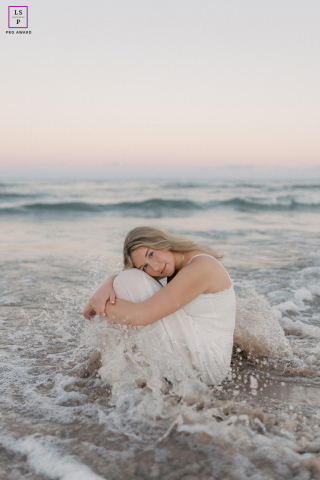 Sheboygan Sunset Serenity: Smiling Girl Surrounded by Gentle Pastel Waves on Lake In Sheboygan, Wisconsin, a smiling teen girl sits in the water at sunset, surrounded by gentle waves and a sky filled with soft pastel colors.