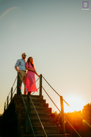 In Mauguio, France, a couple stands at the top of a staircase during sunset, bathed in the warm glow of the evening light.