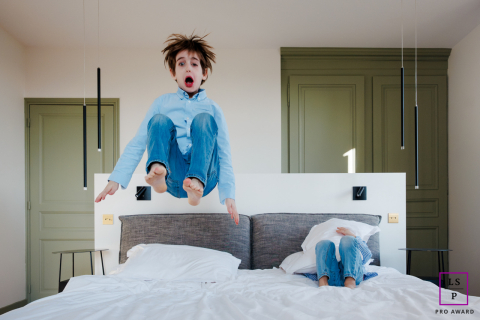 In Paris, two brothers play on a bed; one leaps high with mouth open, captured mid-air in energetic fun.