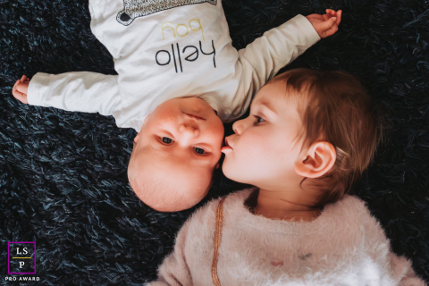 In Annecy, Haute-Savoie, France, a toddler lovingly kisses their baby sibling, capturing a sweet session of sibling affection.
