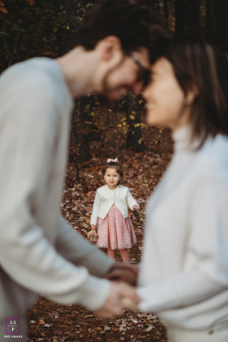 Beloved Boston parents hold hands, heads touching, their young daughter sweetly framed between them.