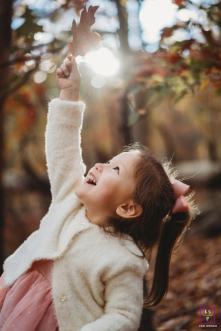 Boston girl reaching high with a single autumn leaf in her hand.