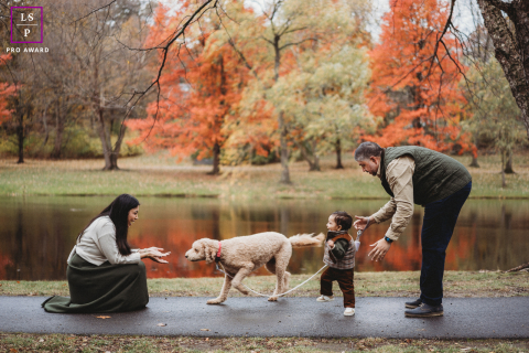 Boston family of three and their dog walk near a park pond during colorful autumn.