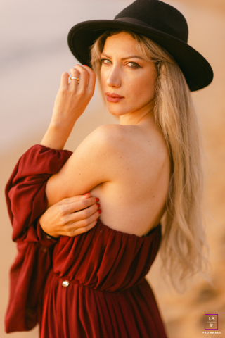 Sunrise lifestyle portrait of a woman in a black hat looking over her shoulder on a Barcelona beach.