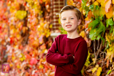 Kid stands posed next to an old brick building covered in vibrant, stunning autumn leaves in Reno, Nevada.