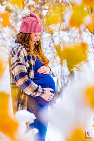 Pregnant woman holding her belly stands happily outdoors in the winter snow of Tahoe City, California.