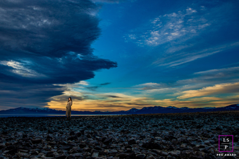 Girl proudly displays her pregnant belly while standing on rocks overlooking snowy Tahoe mountains.