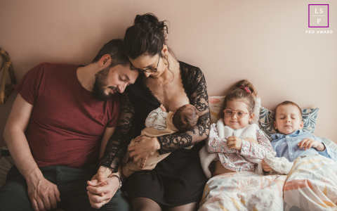 This intimate domestic tableau captures the quiet exhaustion and profound beauty of a growing family, layering the mother’s nurturing focus against the father’s weary lean. It is a masterfully tender scene.