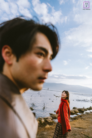 Along the shoreline in Yunnan, the woman smiles brightly in the distance while her companion fills the foreground in thoughtful blur. The unusual focus and wide spacing give the photograph movement, depth, and playful cinematic storytelling.