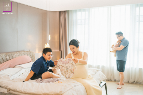 In this Chengdu home, excitement quietly fills the room as the family gathers around clothes prepared for the new baby. The soft window light and layered arrangement of each family member give the photograph warmth, anticipation, and gentle everyday joy.