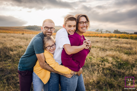 In the open countryside near Lyon, this family squeezes together so tightly they resemble one joyful human sandwich. The playful stacking of arms, smiles, and faces gives the photograph humor, warmth, and wonderfully unfiltered family affection.