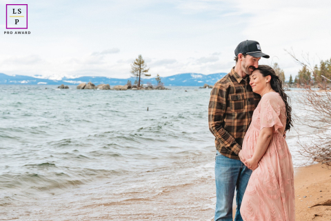 Expecting Couple Stands Together On Shoreline With Calm Anticipation At Lake Tahoe, California Along the shoreline of Lake Tahoe, this expecting couple stands quietly together as wind and water soften the scene around them. The open landscape and muted tones give the photograph calmness, intimacy, and a beautiful sense of anticipation.