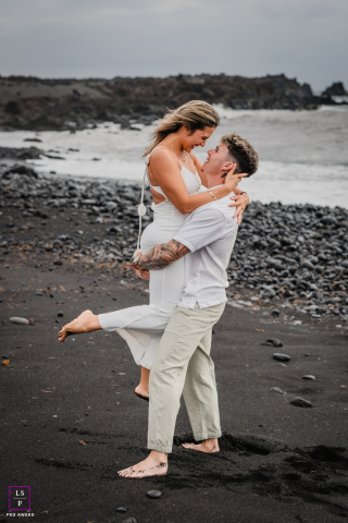 On the dark shoreline of Lanzarote, the couple clings to each other as wind and waves sweep around them. The muted coastal tones and lifted embrace give the photograph movement, romance, and the feeling of love resisting the storm.