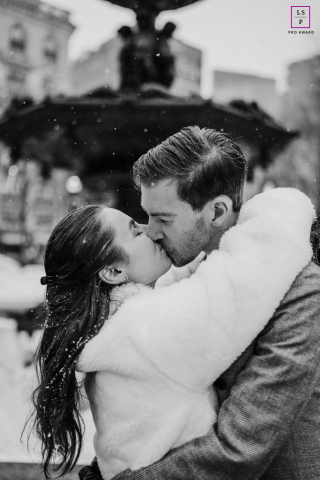 Snow falls softly around this Boston couple as they disappear completely into the kiss, unaware of the city beyond them. The black and white tones and blurred fountain background give the photograph timeless romance and quiet cinematic beauty.