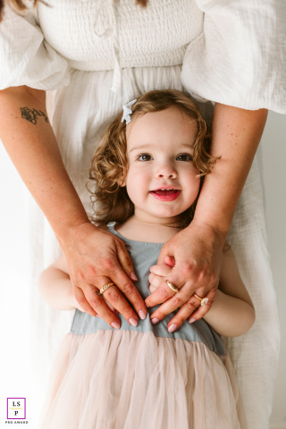 In Chicago, Illinois, a mother gently wraps her hands around her daughter in a tender close-up filled with warmth. The soft tones and quiet embrace highlight their bond, creating a heartfelt portrait of love and connection.