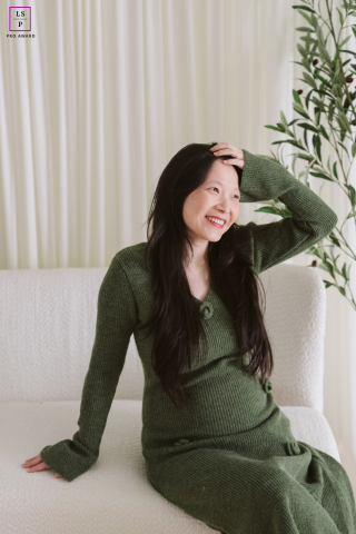 In Norwood, New Jersey, the expectant mother smiles softly while surrounded by calming neutral tones and gentle window light. Her relaxed pose and rich green dress bring warmth and elegance to the portrait, creating a quiet celebration of motherhood.