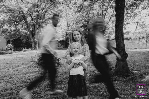 Two young girls stand calmly together as their parents rush past in motion during a playful family session in Loire, France.